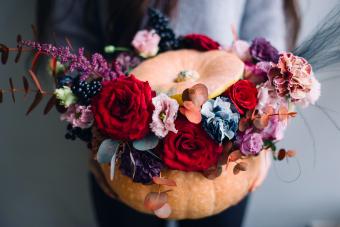 Woman holding orange carved pumpkin filled with blossoming flowers in a halloween themed design