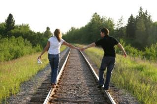 Couple holding hands walking on train tracks