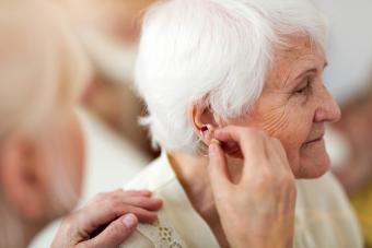 Doctor applying hearing aid to senior woman's ear