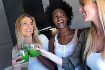 Pretty young women toasting with detox green juice and smiling at home