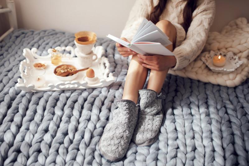 Woman with long hair drinking hot coffee and reading book in bed