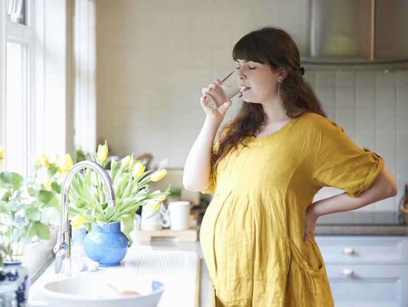 pregnant woman drinking water in her kitchen