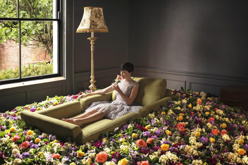 Woman sitting on sofa surrounded by flowers