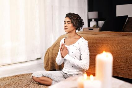 Young woman sitting and meditating with candles in her living room at home