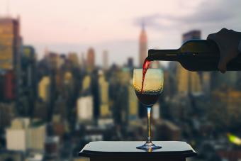 Hand with bottle pours red wine into glass on Manhattan background