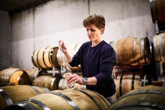 Female vintner in wine cellar pouring wine into glass