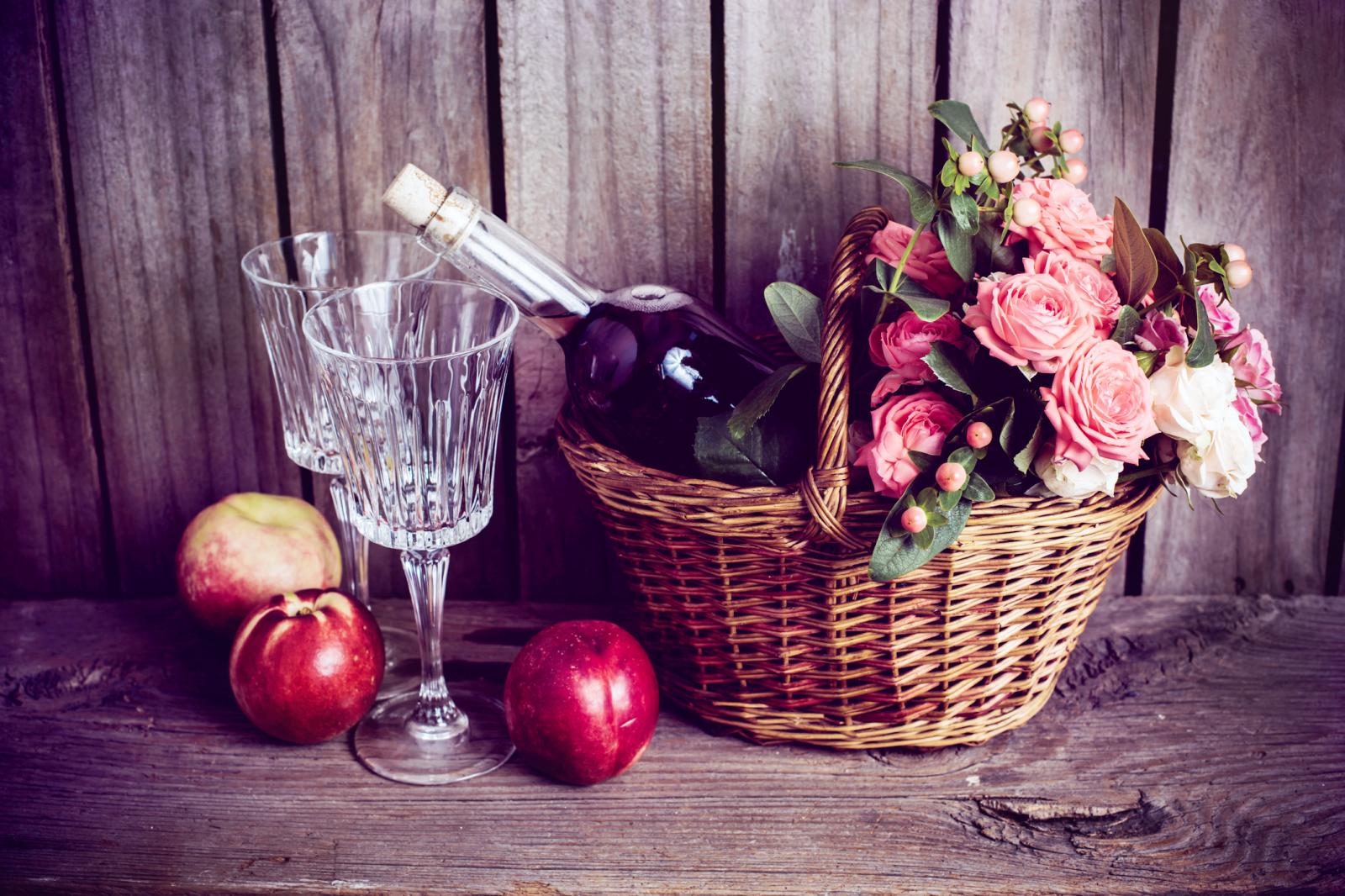 wicker basket and a bottle of rose wine with two wineglasses and nectarines