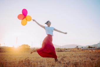 Young woman wearing a red maxi skirt running threw the field holding balloons 