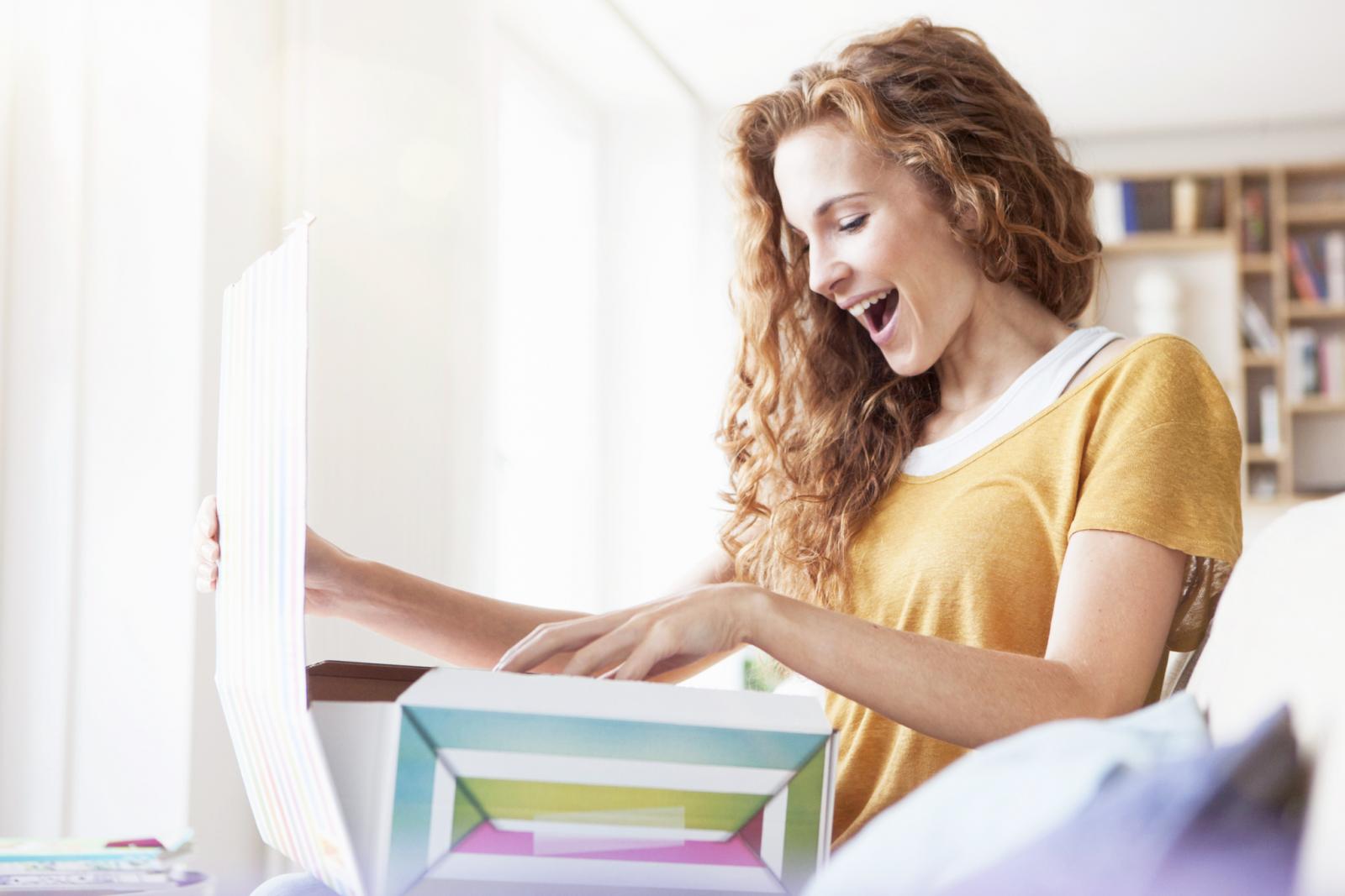 Happy woman at home sitting on couch unpacking parcel
