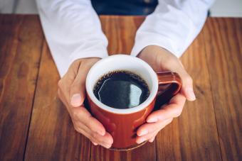 Someone hands holding a mug of black coffee before drinking.