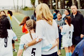 Mother embracing young female soccer player on sidelines after game