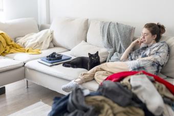 Young woman sitting on the couch with her cat surrounded by laundry