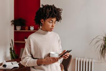 looking intently at phone and posing in office with white cup