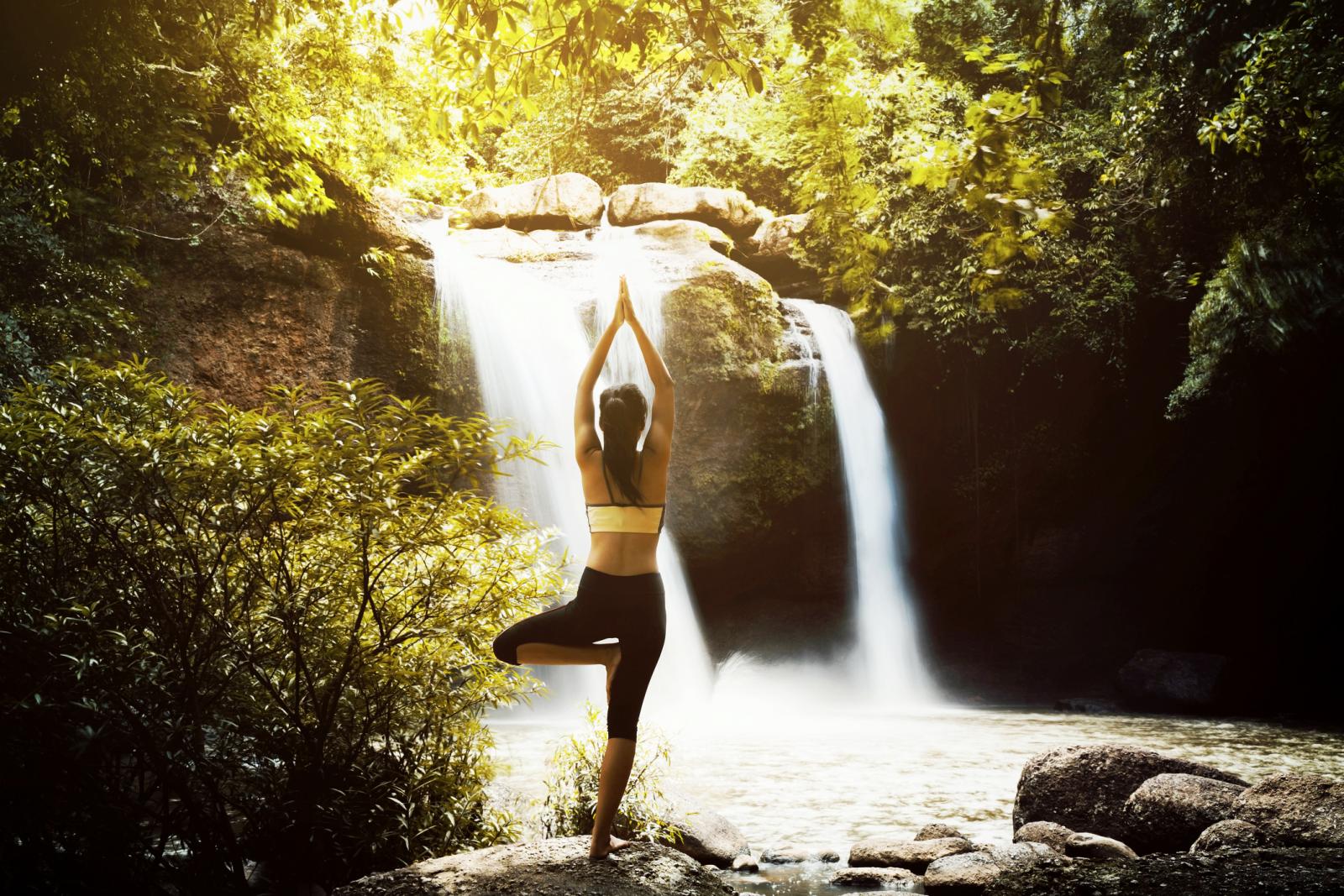 Woman Doing Tree Pose Yoga Against Waterfall