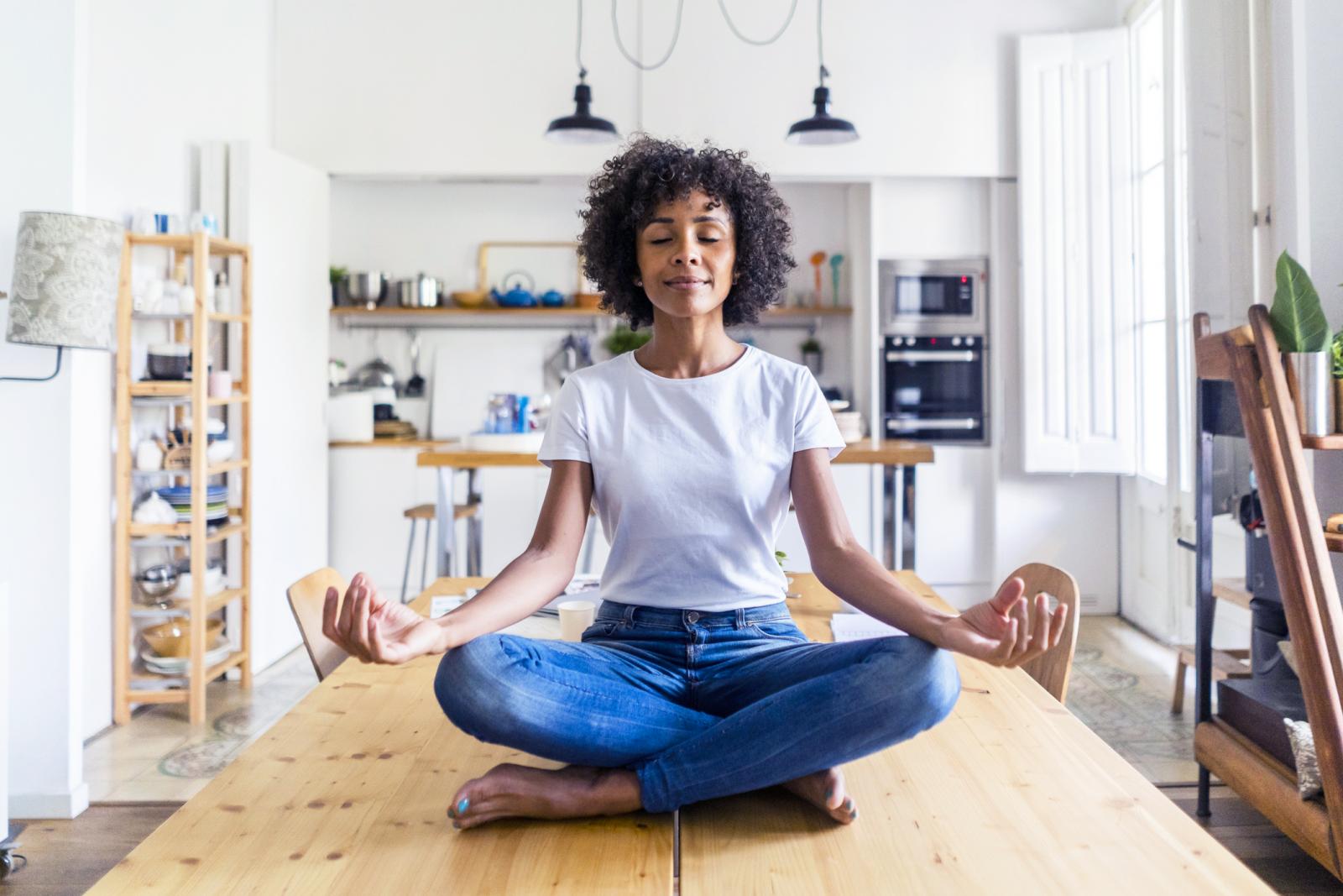 Smiling woman with closed eyes in yoga pose on table at home